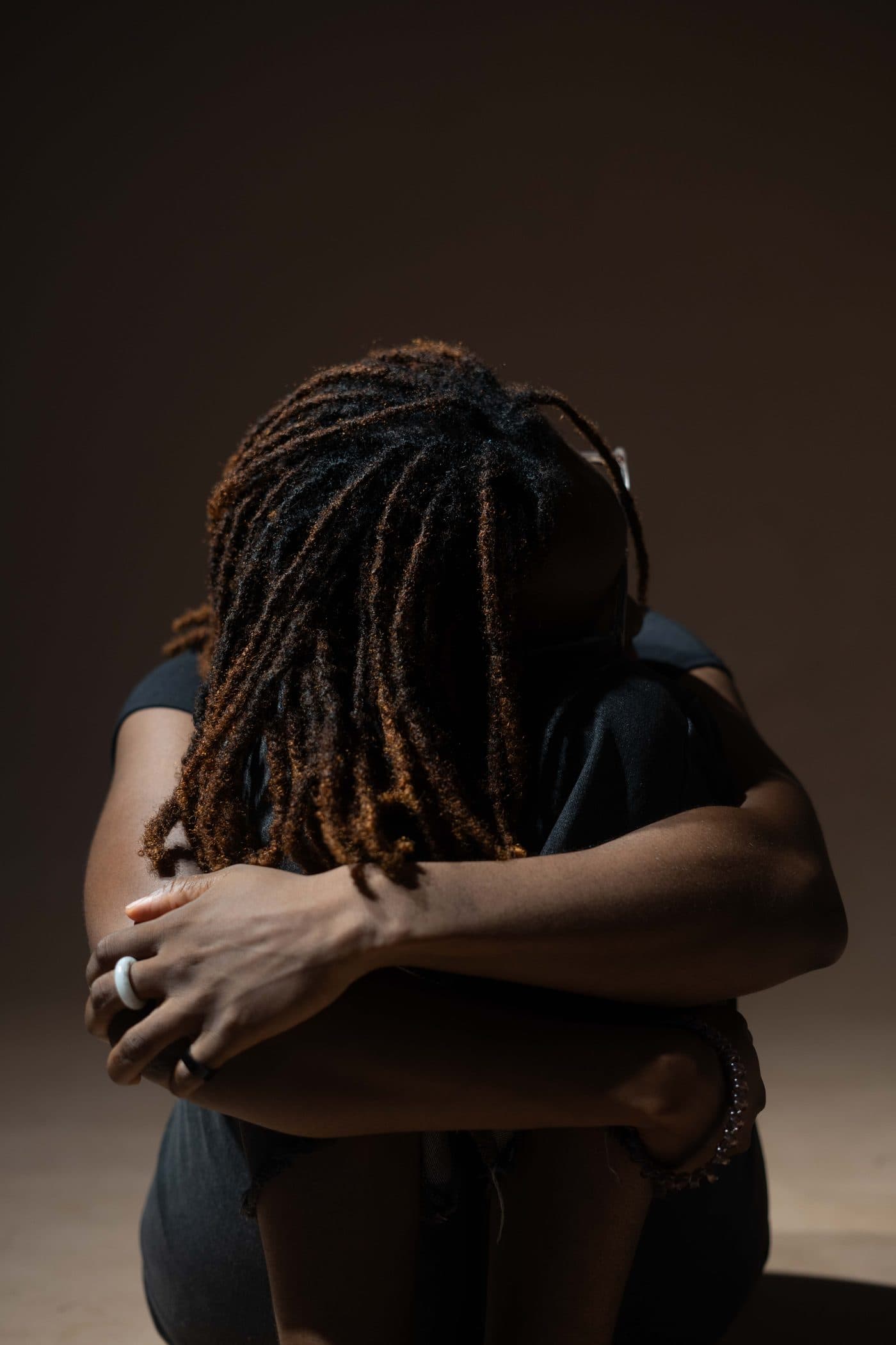 A person sitting on the floor with their knees drawn in and head resting down, in a quiet, reflective moment